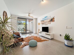 A modern living room with a flat-screen TV, leather sofa, and a large window. - Family Oasis: Vacation rental with a 140 m² terrace, pool, and just 5 minutes from the beach (AN)
