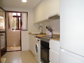 A compact kitchen with a washing machine, oven, and a sink with utensils. - Apartment sea view, AC and parking - 6 guests (Gandia)
