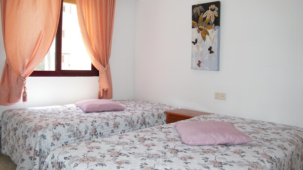 Ein Schlafzimmer mit zwei Betten, Pfirsichfarbenen Vorhängen, einer blumigen Tagesdecke und einem Wandbild.