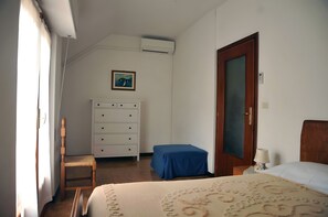 Een slaapkamer met een bed, een houten stoel, een dressoir, een blauwe tafel en een deur.