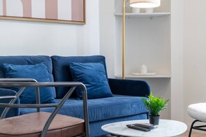 A modern living room with a blue sofa, a metal-framed chair, a small round table with a remote control, and a potted plant. - B3. Two Bedrooms#Champs-Élysées#Arc de Triomphe#AC (Paris)