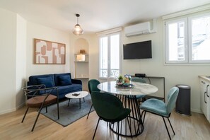 Ein modernes Wohnzimmer mit einem blauen Sofa, einem runden Tisch mit Stühlen, einem Couchtisch und einem an der Wand befestigten Fernseher.