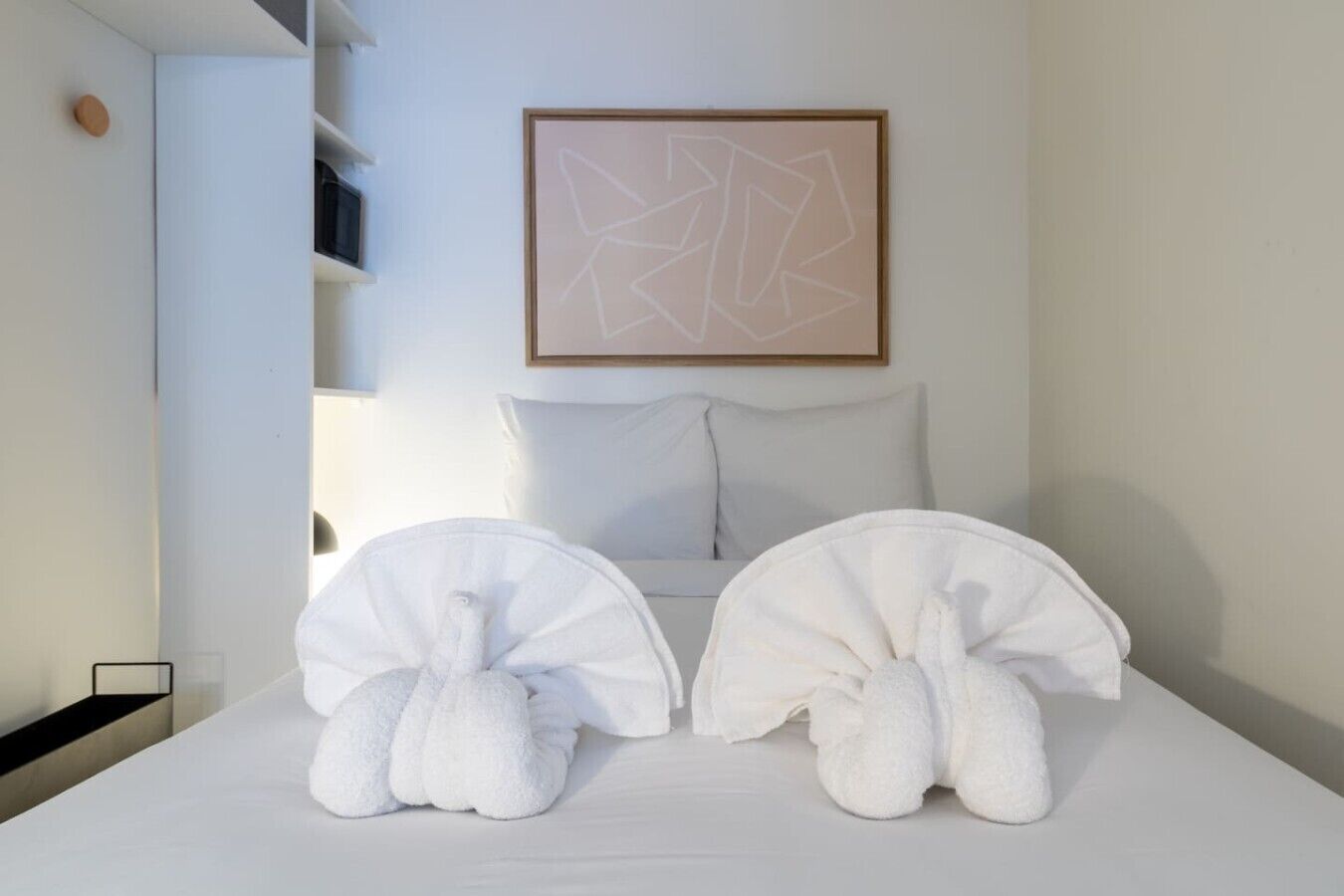 Ett hotellrum med en säng, kuddar, ett inramat abstrakt konstverk och två handdukar formade som djur.