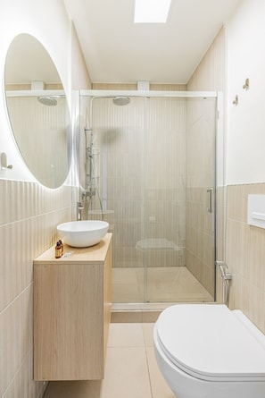 A modern bathroom with a glass-enclosed shower, a freestanding toilet, and a vanity with a sink. - Arc de Triomphe - Bail Mobilité - Place Victor Hugo - 2-bedroom (Paris)