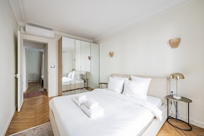 A hotel room with a large bed, a bedside table, a lamp, a mirror, and a view of the hallway. - Arc de Triomphe - Bail Mobilité - Place Victor Hugo - 2-bedroom (Paris)