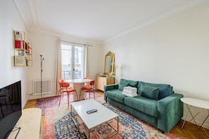 A living room with a green sofa, a round coffee table, a white table, and a red chair. - Arc de Triomphe - Bail Mobilité - Place Victor Hugo - 2-bedroom (Paris)