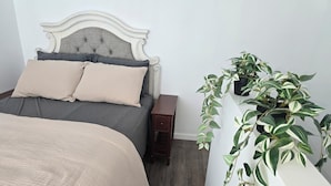Un dormitorio con una cama, una mesita de noche, un aparador y una planta en maceta.