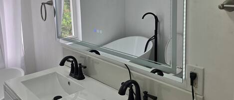 A modern bathroom with two sinks, a large mirror, and a window.