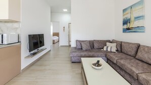 En moderne stue med et fladskærms-tv, en sofa, et sofabord og et maleri af en sejlbåd.