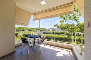 Een balkon met een tafel en stoelen, uitzicht op groen en gebouwen, en een witte balustrade.