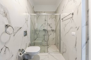Een badkamer met een glazen douchecabine, toilet en marmeren wanden.
