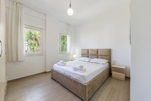 Ein helles, modernes Schlafzimmer mit einem Holzbett, zwei Nachttischen und einem Fenster mit Vorhängen.