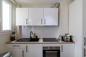 A compact kitchen with white cabinets, a black countertop, a sink, a stove, and a window. - B2. Two Bedrooms#Champs-Élysées#Arc de Triomphe#AC (Paris)