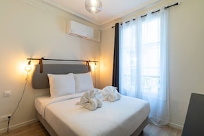 A hotel room with a bed, a wall-mounted air conditioner, a window with curtains, and a light fixture. - B2. Two Bedrooms#Champs-Élysées#Arc de Triomphe#AC (Paris)
