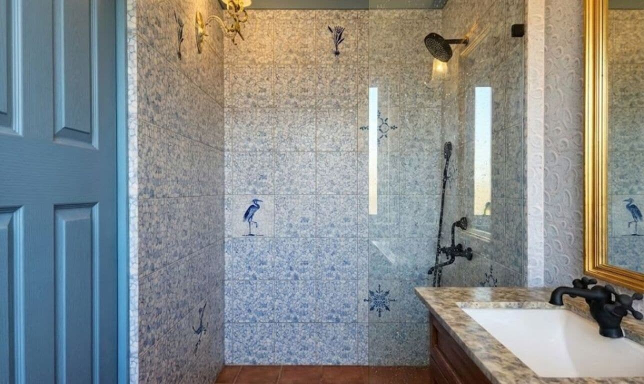 A bathroom with a marble wall, a sink with a black faucet, and a mirror with a gold frame.