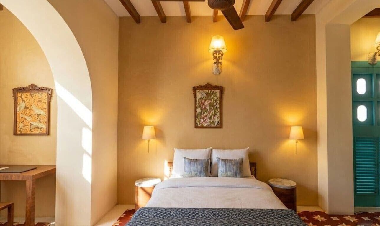 A bedroom with a bed, two bedside lamps, a wall-mounted artwork, and a wooden ceiling fan.