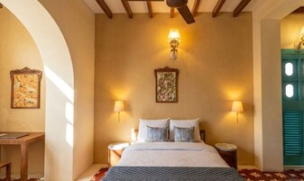 Un dormitorio con cama, dos lámparas de noche, un cuadro en la pared y un ventilador de techo de madera.