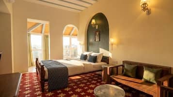 A hotel room with a bed, a sofa, a small table, and a window with curtains.