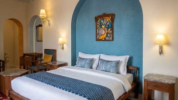 Habitación de hotel con una cama grande, dos mesitas de noche, una silla, un escritorio y una obra de arte colgada en la pared.