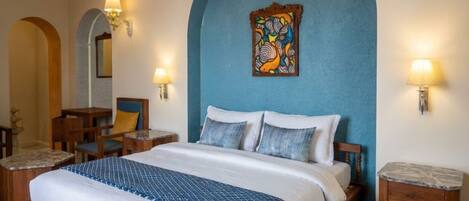 A hotel room with a large bed, two bedside tables, a chair, a desk, and a wall-mounted artwork.