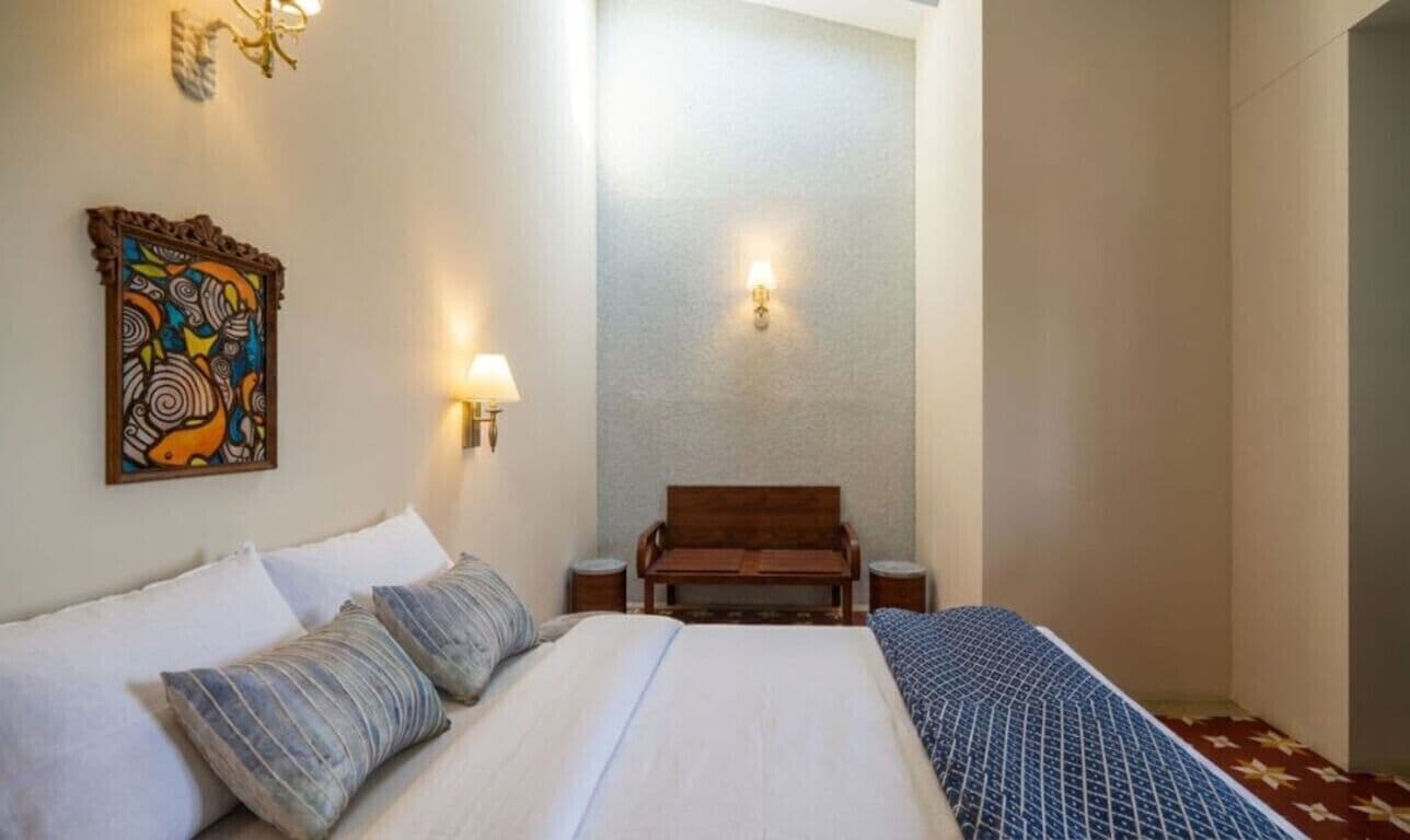 Une chambre d’hôtel comprenant un lit, un banc, une œuvre d’art accrochée au mur et deux appliques murales.