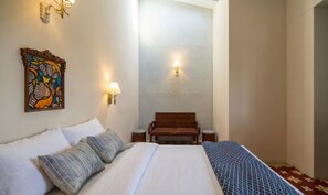 A hotel room with a bed, a bench, a wall-mounted artwork, and two wall sconces.