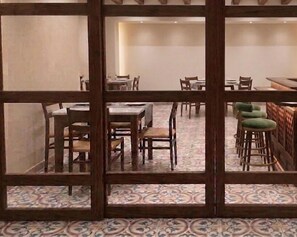 A dining area with tables and chairs, a patterned floor, and a wooden partition. - La Maison Pondichéry (Puducherry)