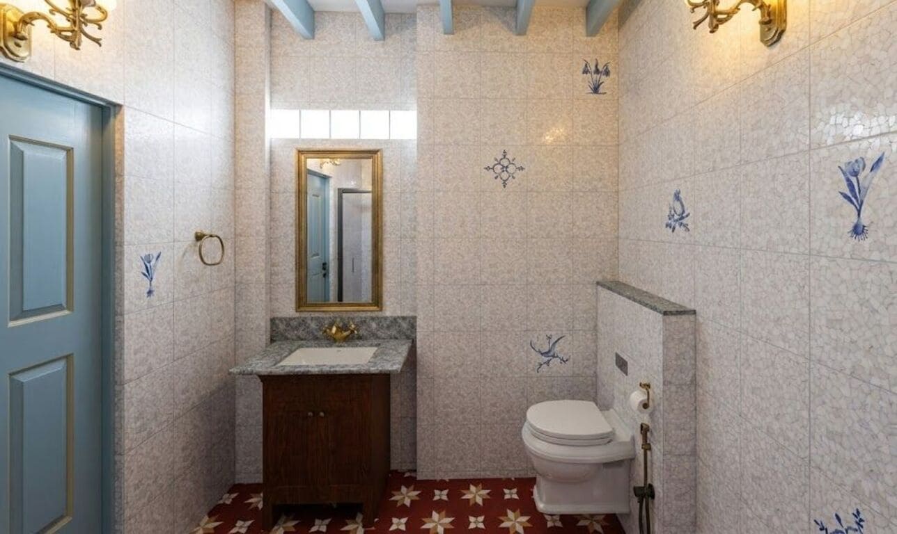 Une salle de bain avec un sol en marbre, des toilettes blanches, un lavabo avec un robinet doré et des carreaux décoratifs.