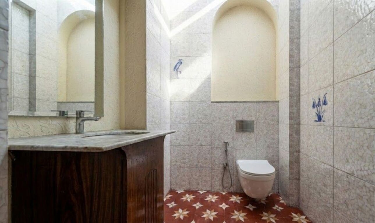 A bathroom with a marble wall, a wooden vanity, a toilet, and a tiled floor with a floral pattern.