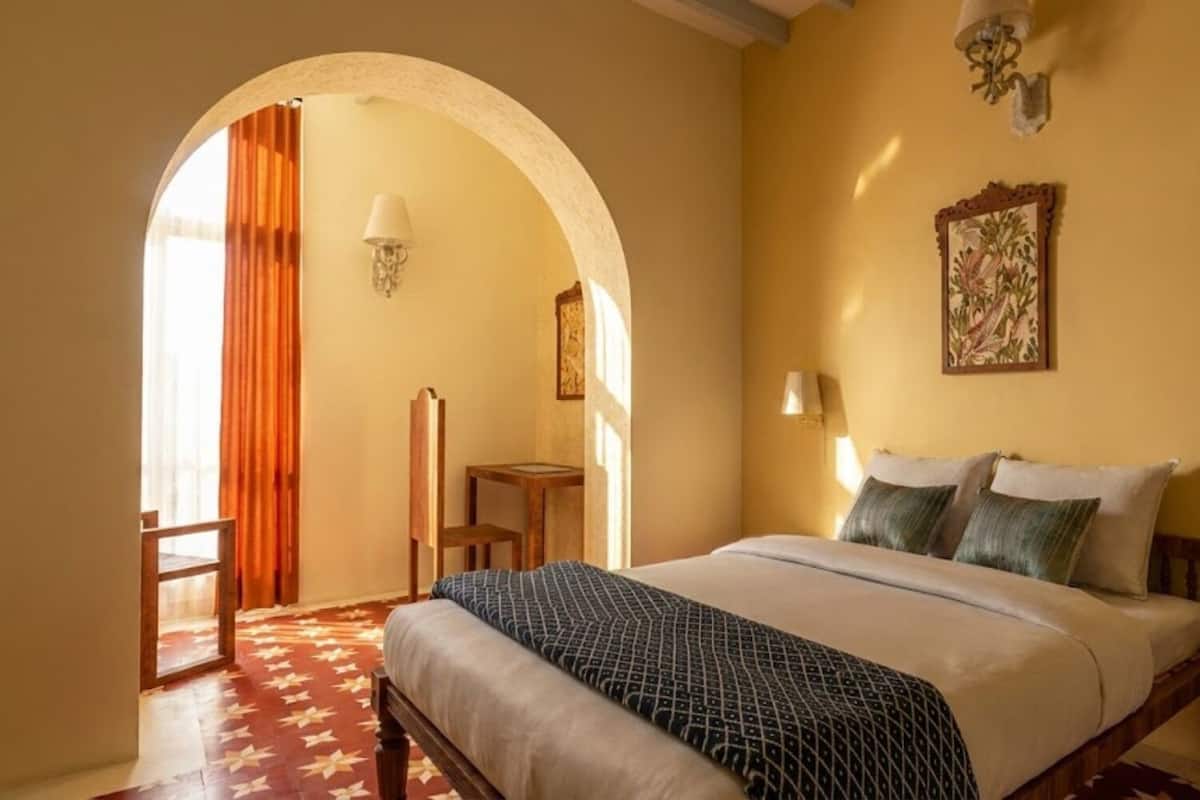 A hotel room with a bed, a chair, a table, and a painting on the wall.