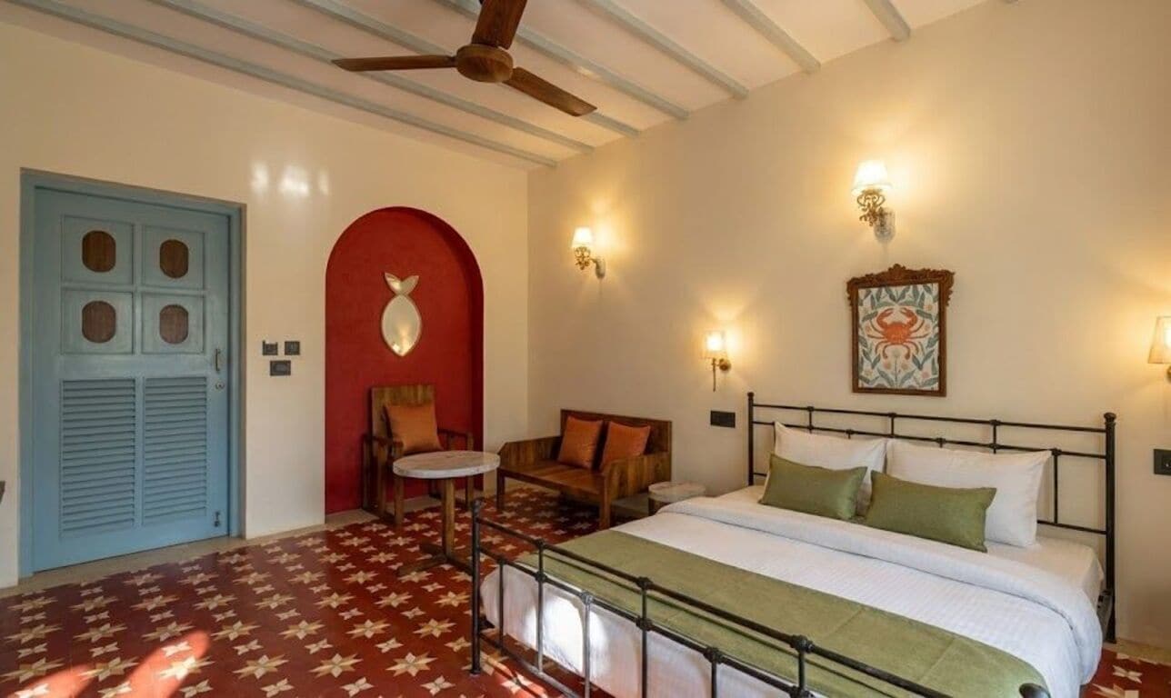 A room with a bed, a chair, a small table, a ceiling fan, and a door.