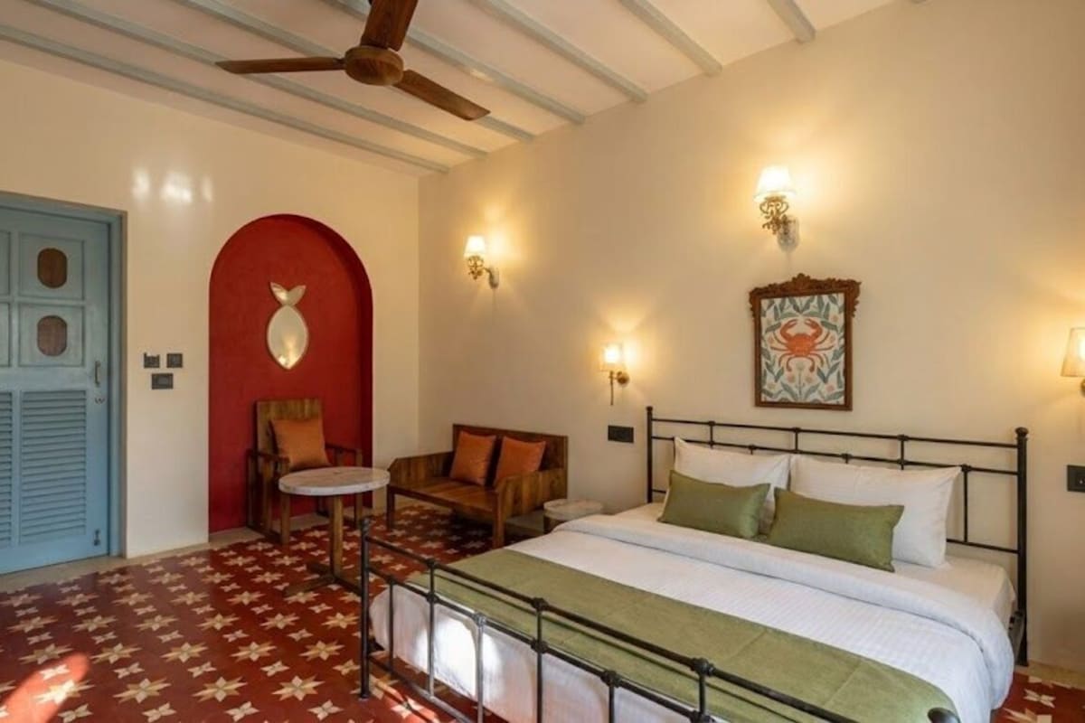 A room with a bed, a chair, a small table, a ceiling fan, and a door.