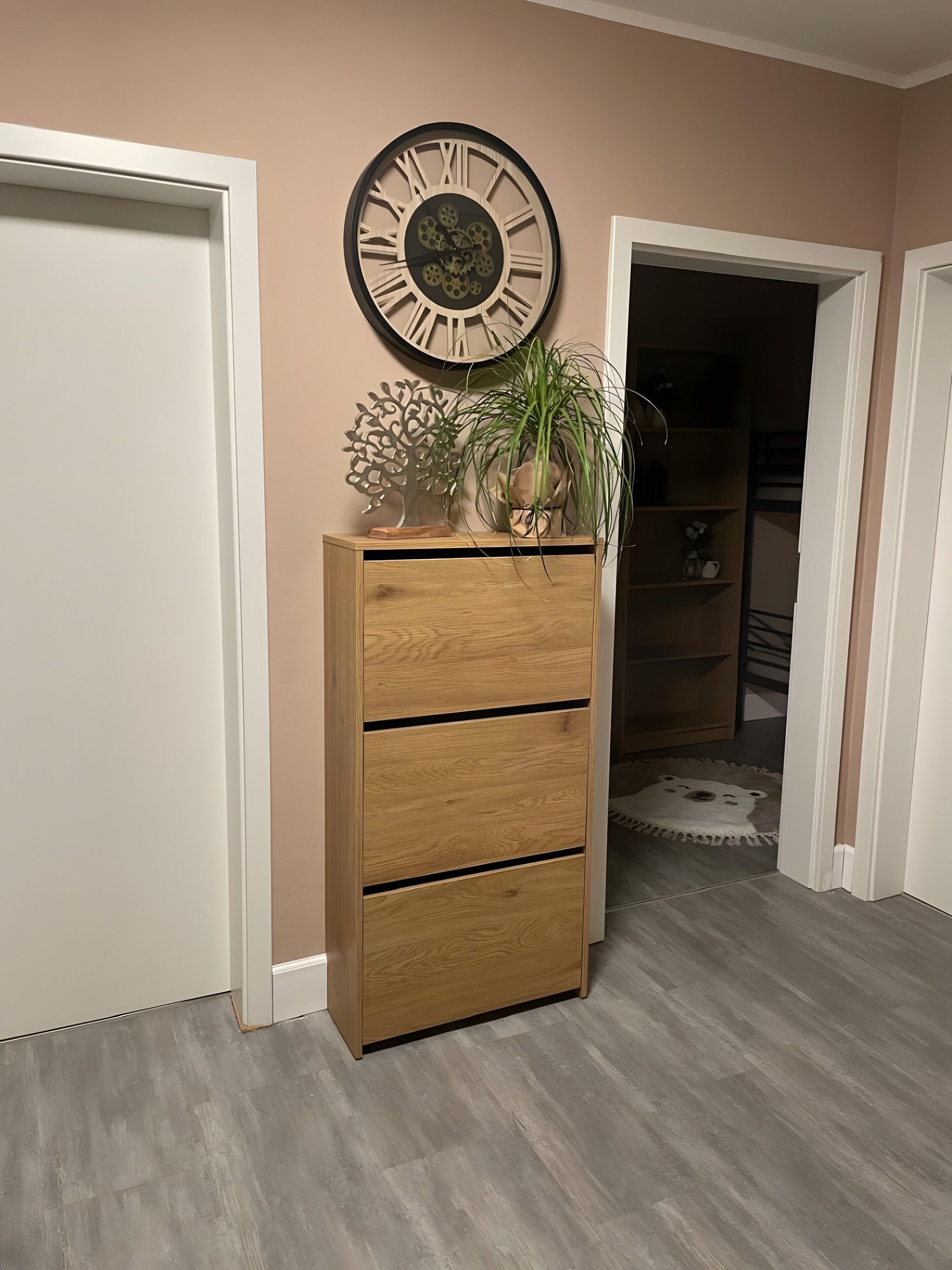 A wooden dresser with three drawers, a wall clock, a potted plant, and a decorative piece on top.