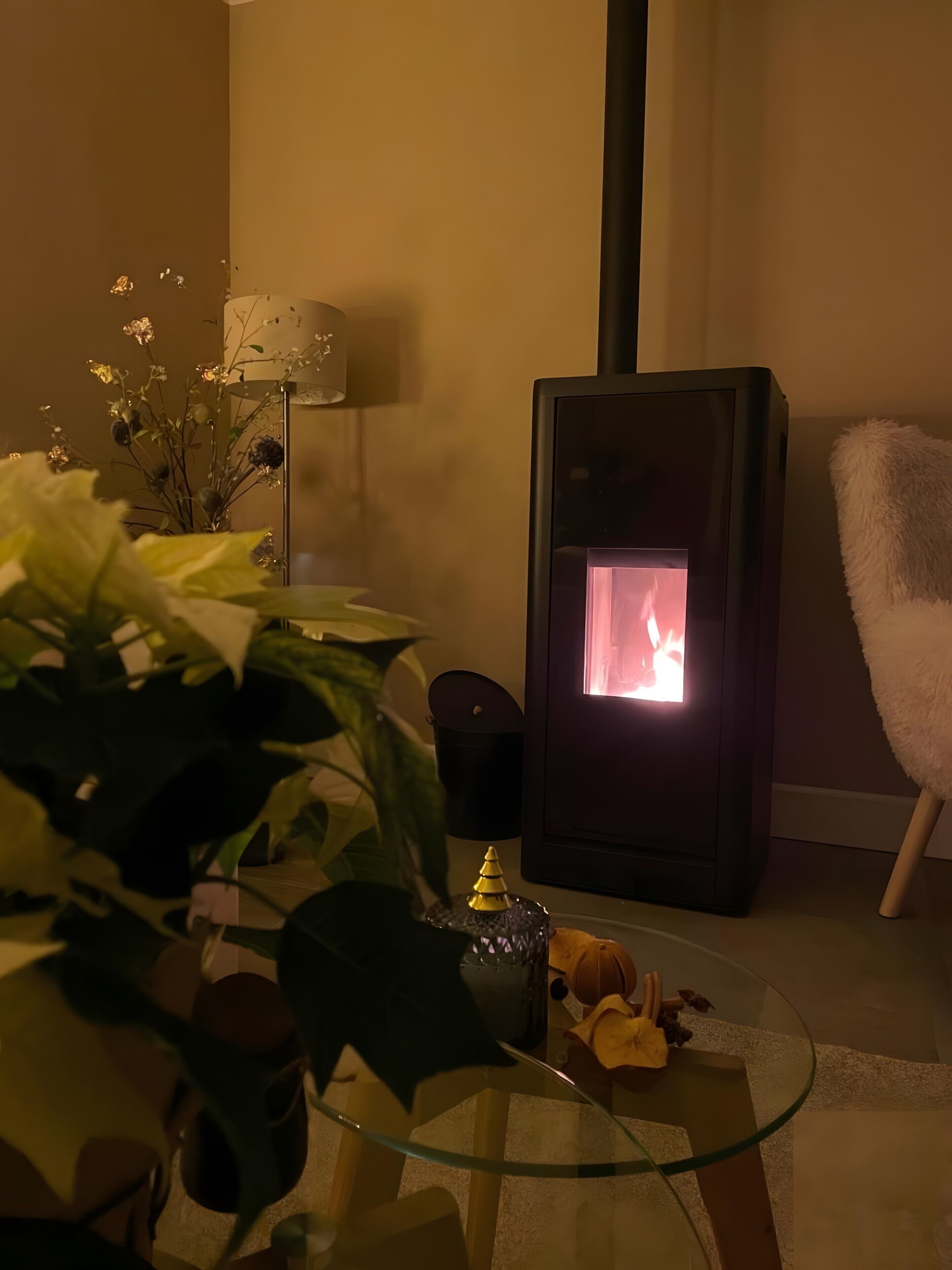 A living room with a glass table, a decorative plant, a small Christmas tree, and a wood-burning stove.