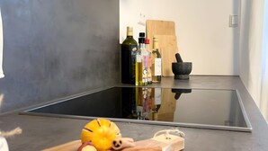 Una cocina de diseño moderno, con encimera negra, tabla de cortar con frutas y especias, y otra tabla de cortar al fondo.