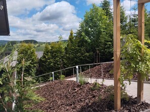 Ein angelegter Gartenbereich mit verschiedenen Bäumen und Sträuchern, einer Holzpergola und einem Metallgeländer.