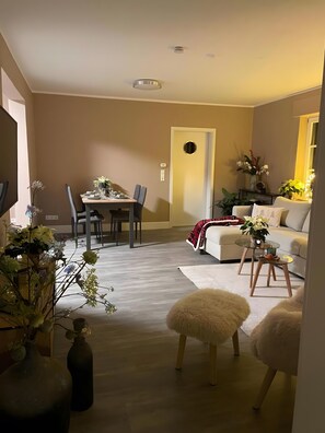 A modern living room with a dining area, a sofa, a coffee table, and decorative plants.