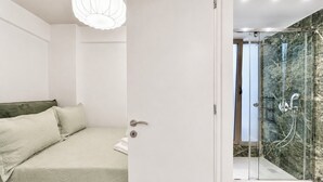 Un dormitorio moderno con cama, una puerta que da a zona de ducha con puertas de cristal y pared de mármol.