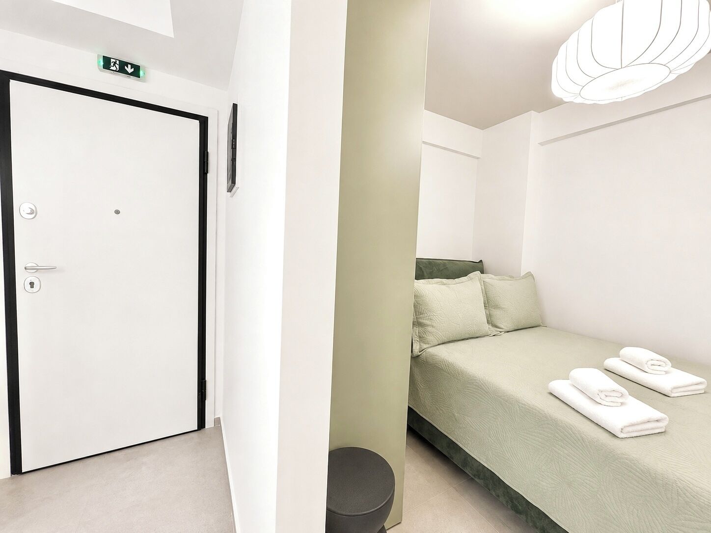 A hotel room with a bed, a toilet, a sink, and a door with an emergency exit sign.