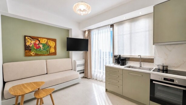 Una sala de estar moderna con un sofá, un televisor, una cafetera y una cocina con estufa y fregadero.