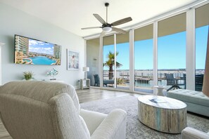 Ein geräumiges Wohnzimmer mit einem großen Flachbildfernseher, einem Deckenventilator und einem Balkon mit Blick auf das Wasser.
