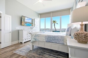 Ein Schlafzimmer mit Bett, Nachttisch, Lampe, Kommode, einem Gemälde und Blick auf den Ozean.