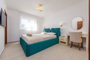 Ein Schlafzimmer mit Bett, Nachttischen, Schreibtisch, Stuhl, Fernseher und Fenster.