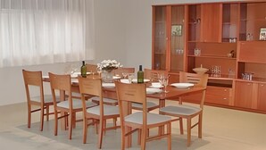 Ein Essbereich mit Holztisch und Stühlen, einer Vase mit Blumen und einem Schrank mit Gläsern.