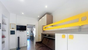 Een compacte kamer met een stapelbed, een televisie, een kitchenette en een eethoek.