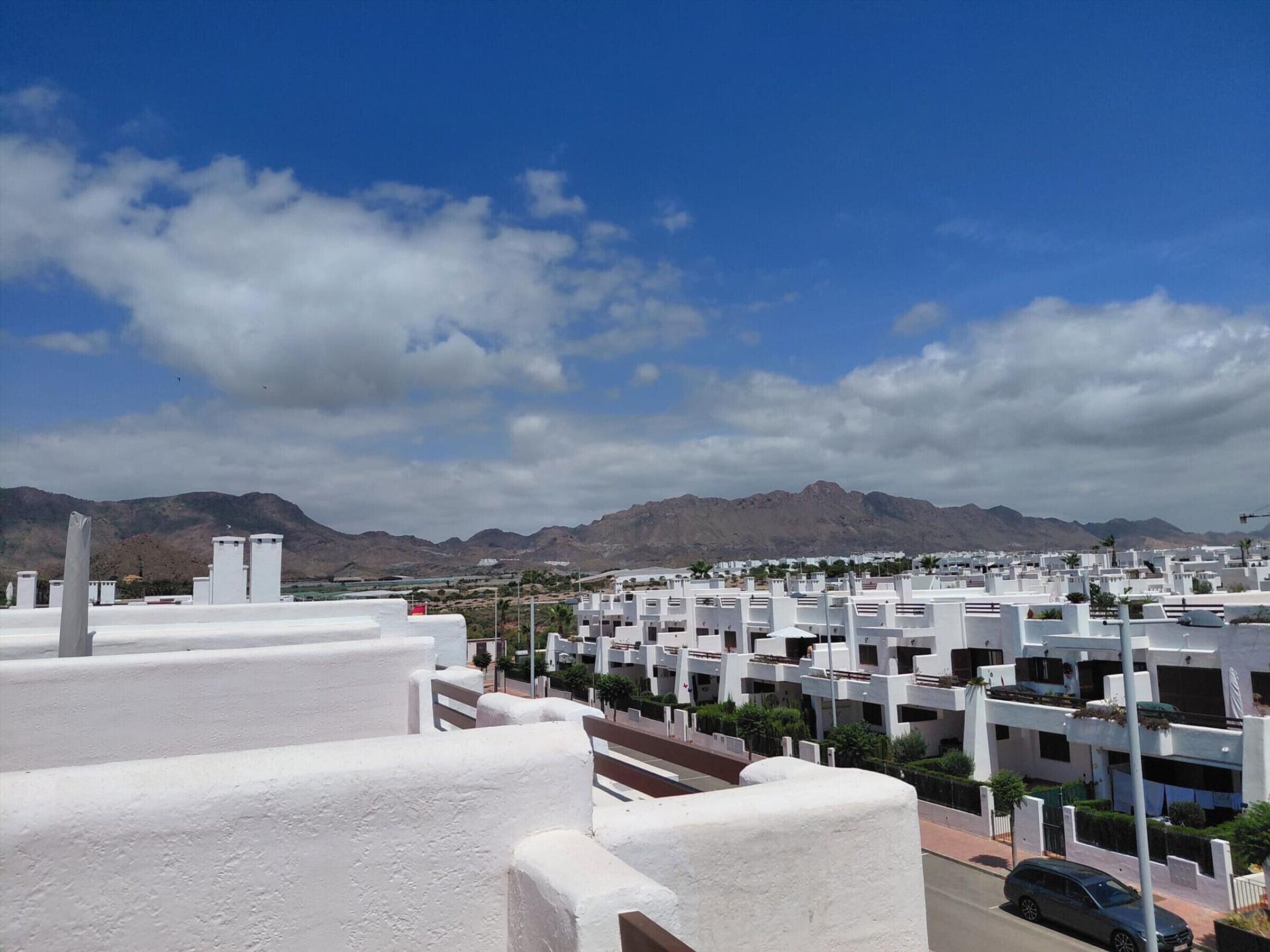 A residential area with white buildings, a clear sky, and mountains in the background.