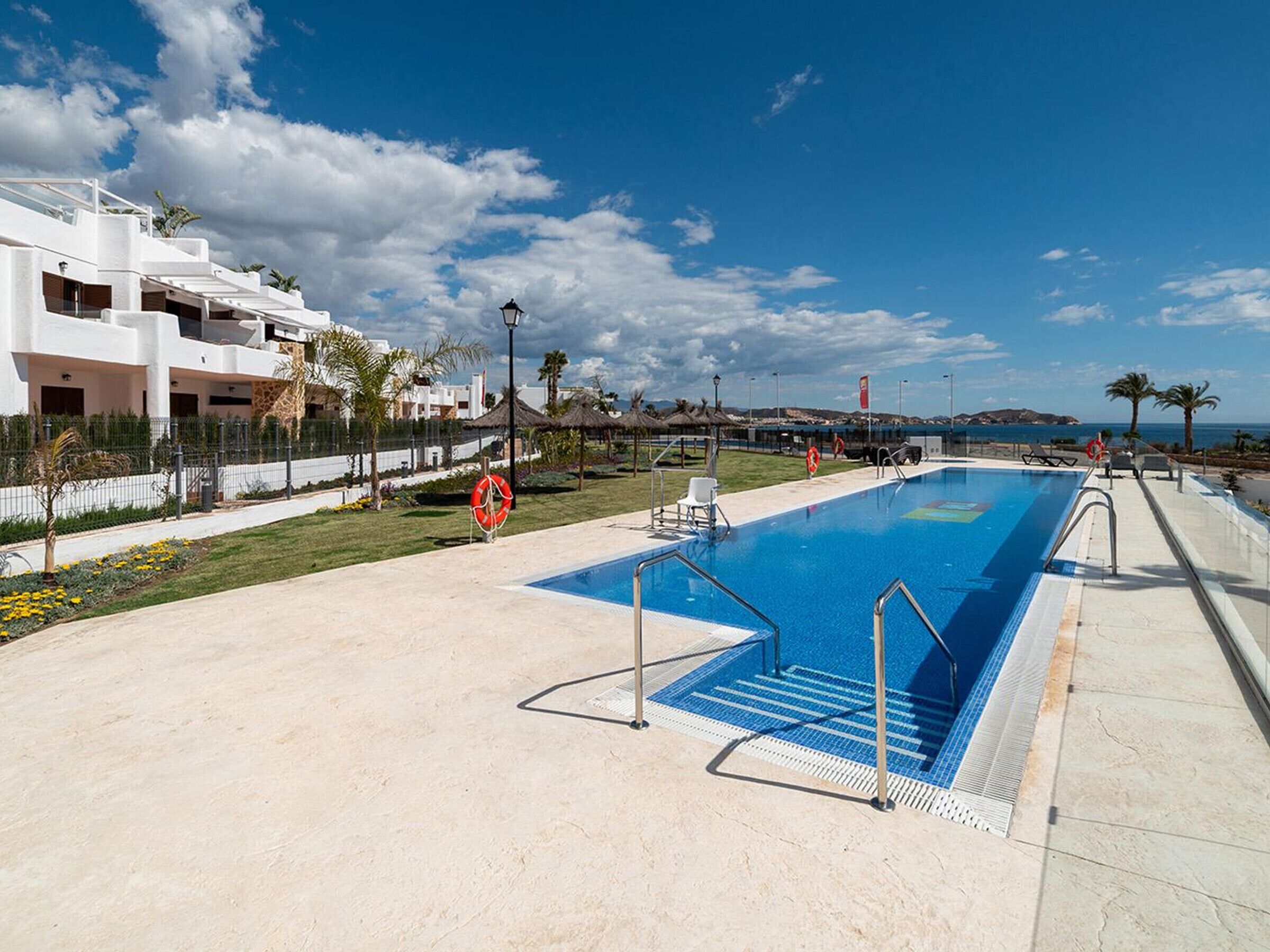 A swimming pool with a lifebuoy, a clear sky, and a building with a white facade.