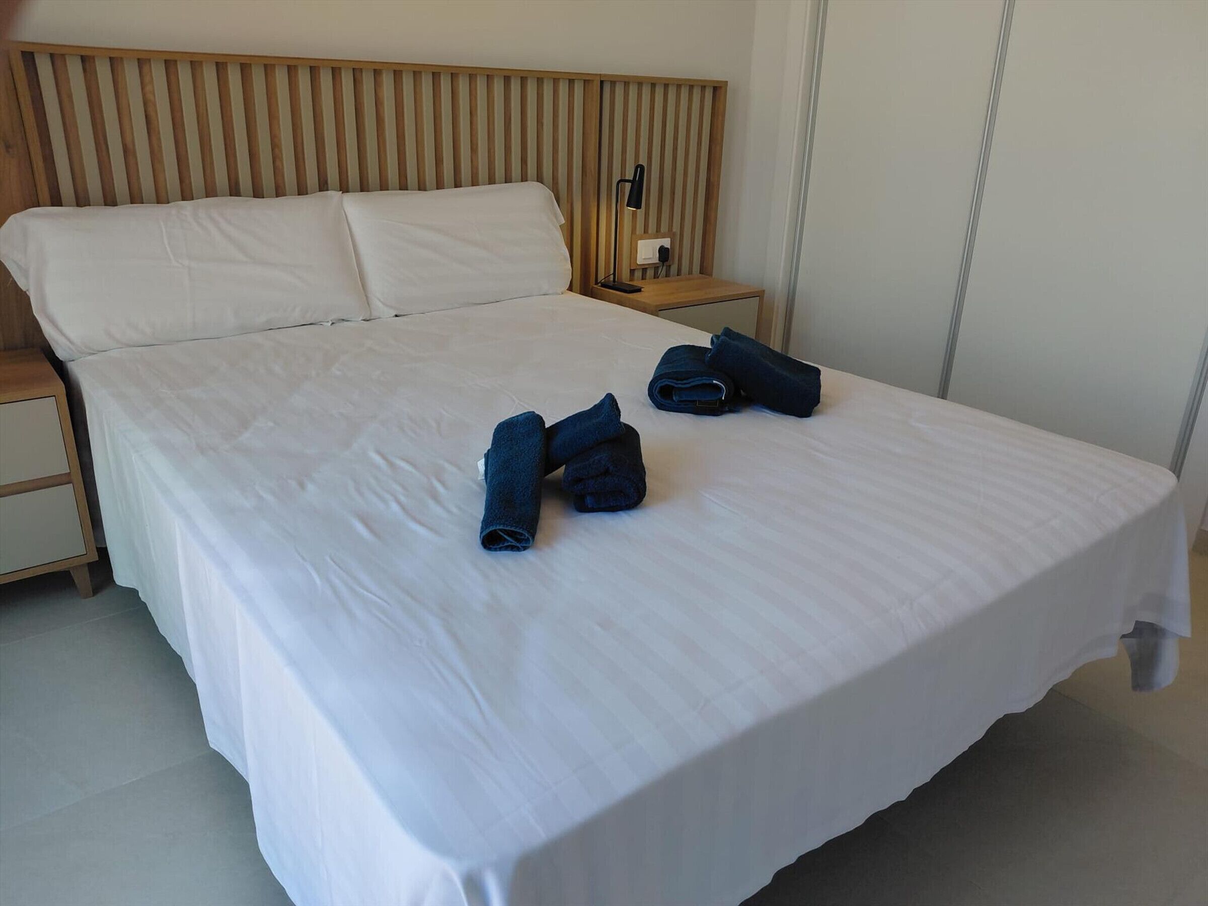 A neatly made bed with white linens, a wooden headboard, and a bedside table with a lamp.