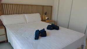 En pænt redt seng med hvide hør og et trægavle samt et natbord med lampe.