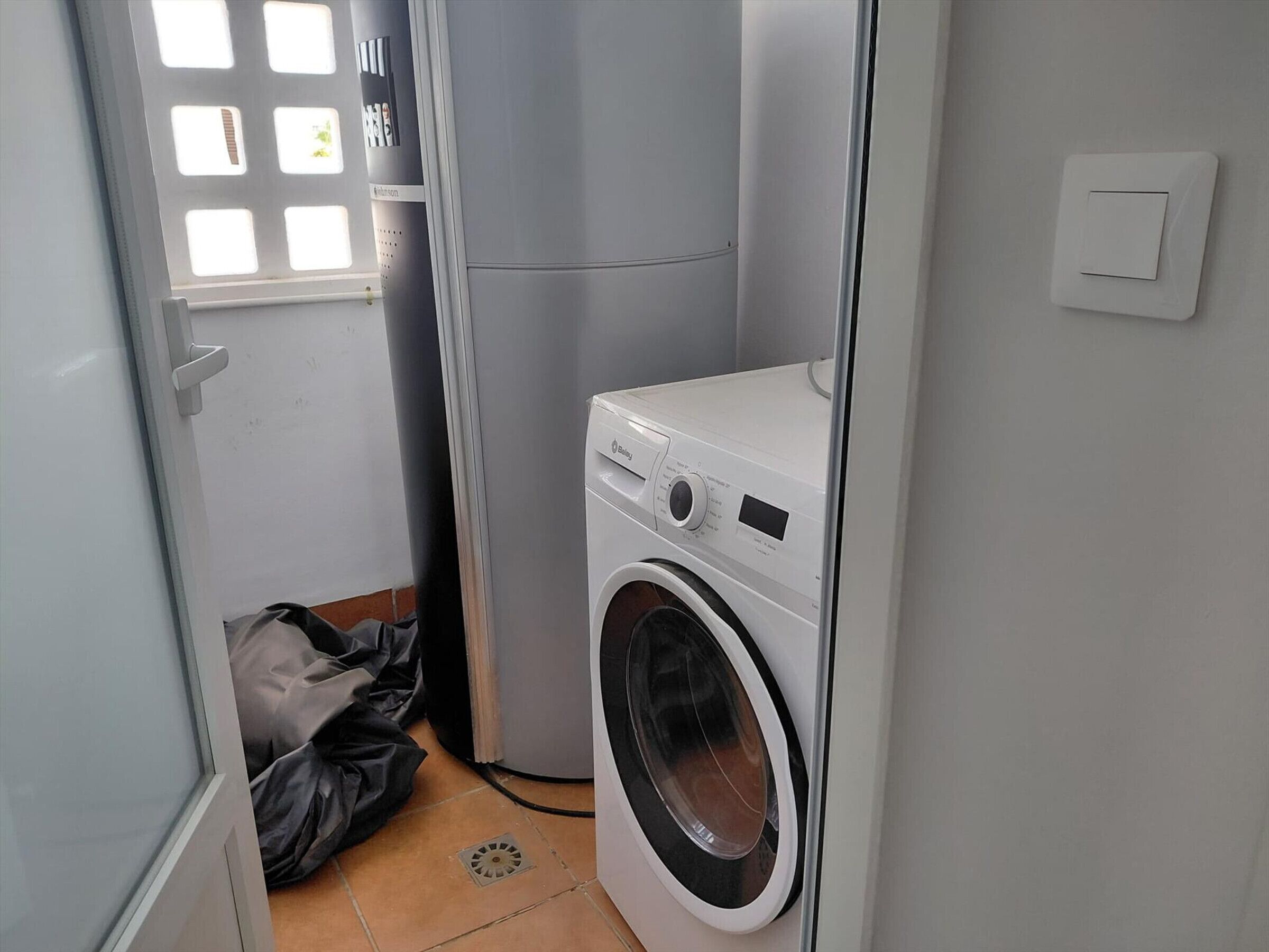 A compact laundry room with a front-loading washing machine, a dryer, and a window with a grid pattern.
